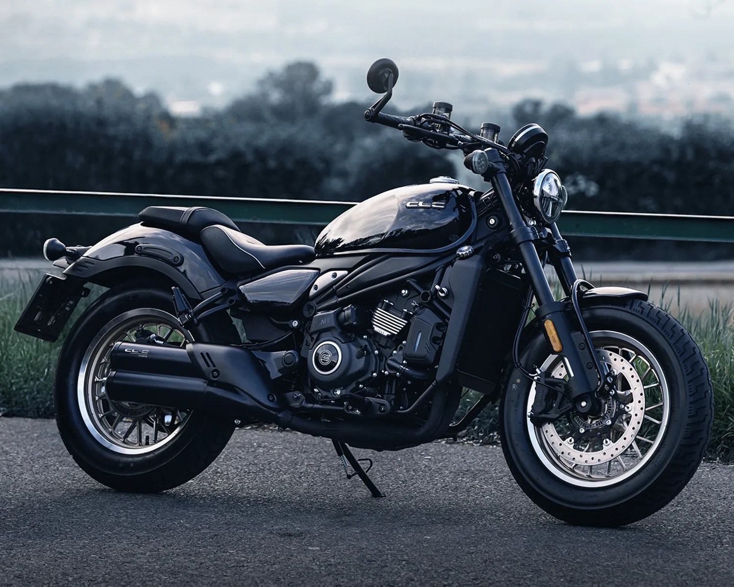 Glossy black cruiser motorcycle parked on a paved road with a blurred natural background.