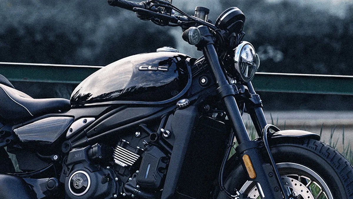 Glossy black motorcycle fuel tank with "CLC" logo and front headlight in an outdoor setting.