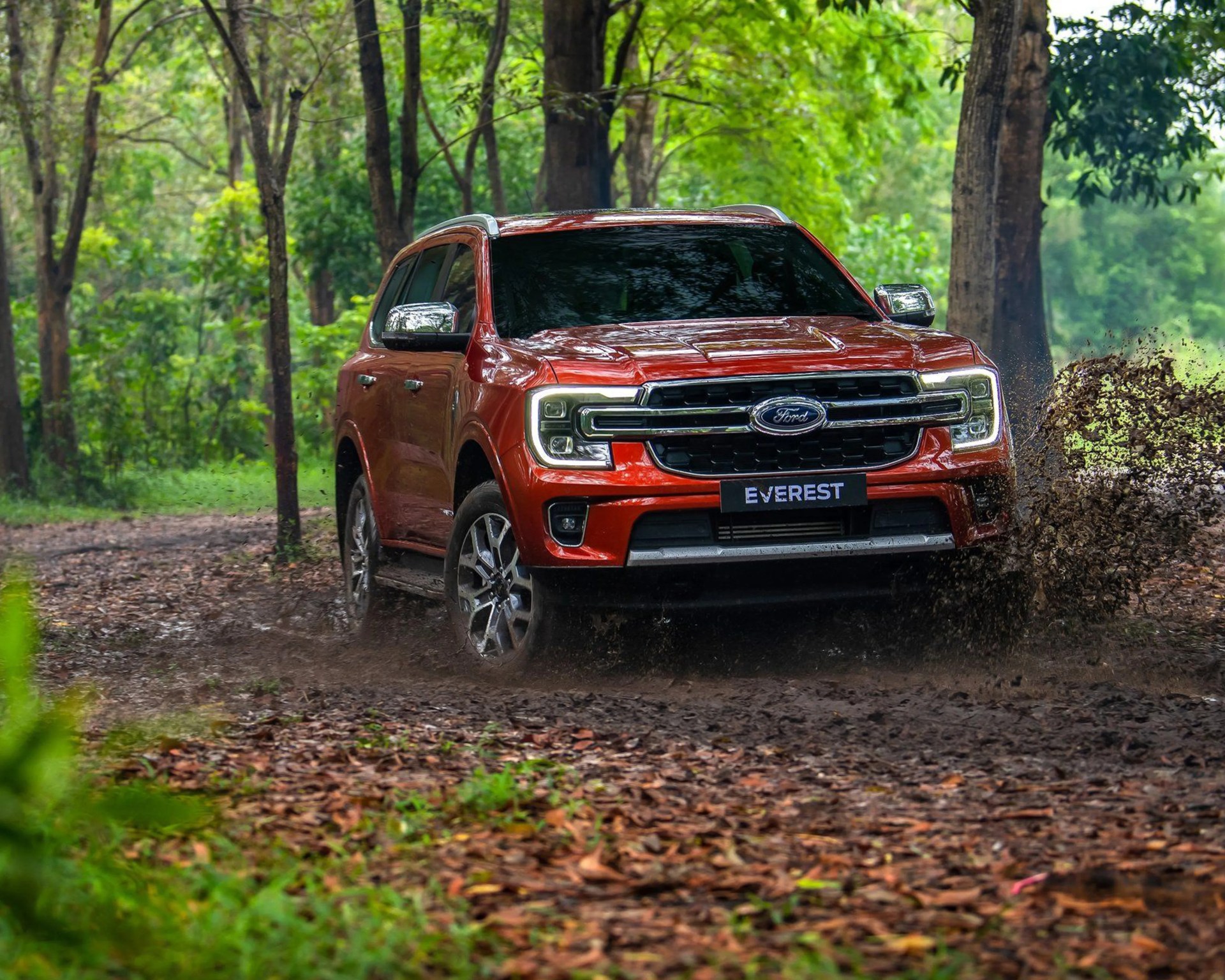 Red Ford Everest SUV splashing mud on a forest trail.