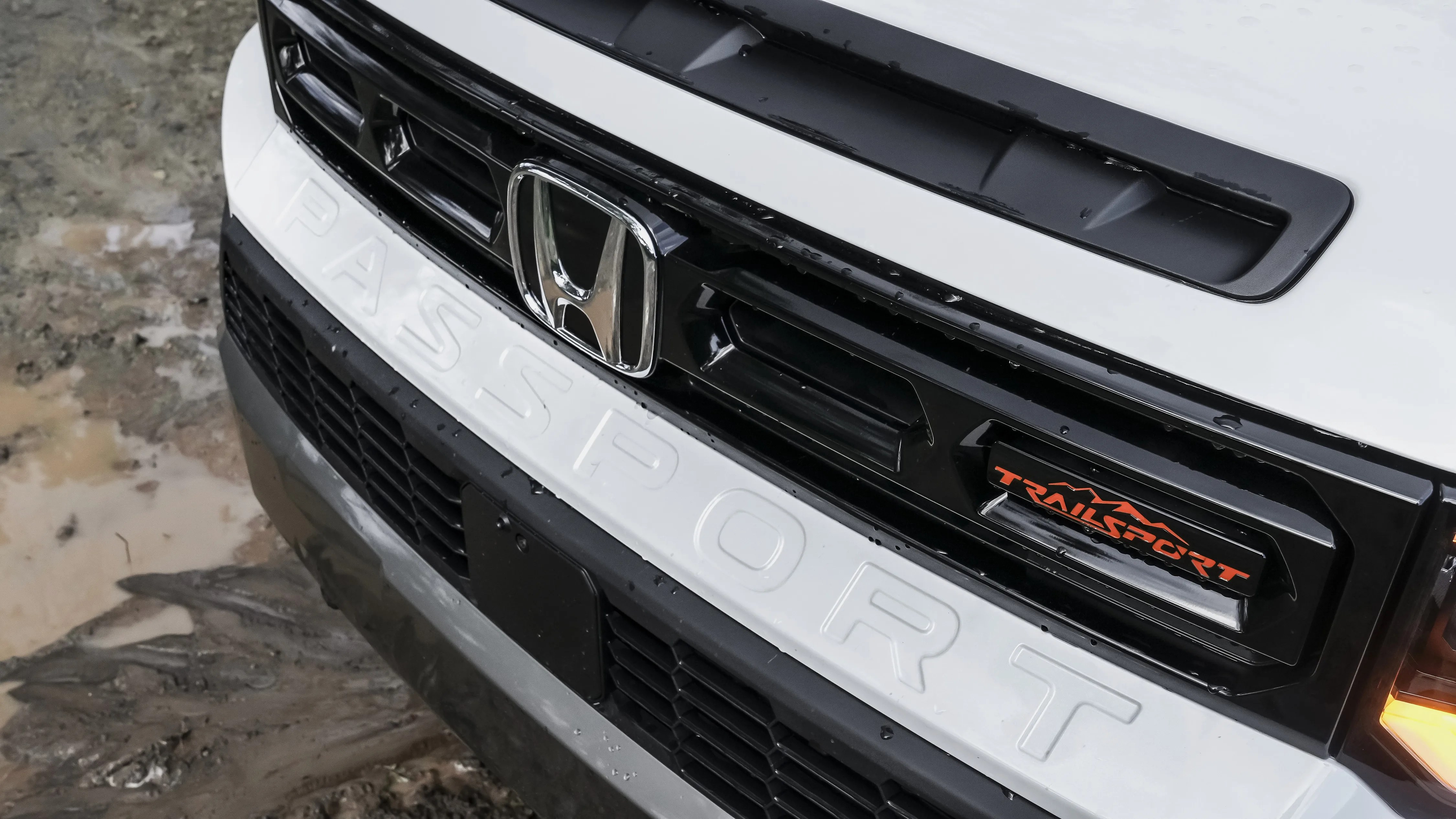Front grille of a white Honda Passport Trailsport with black accents and orange Trailsport badge.