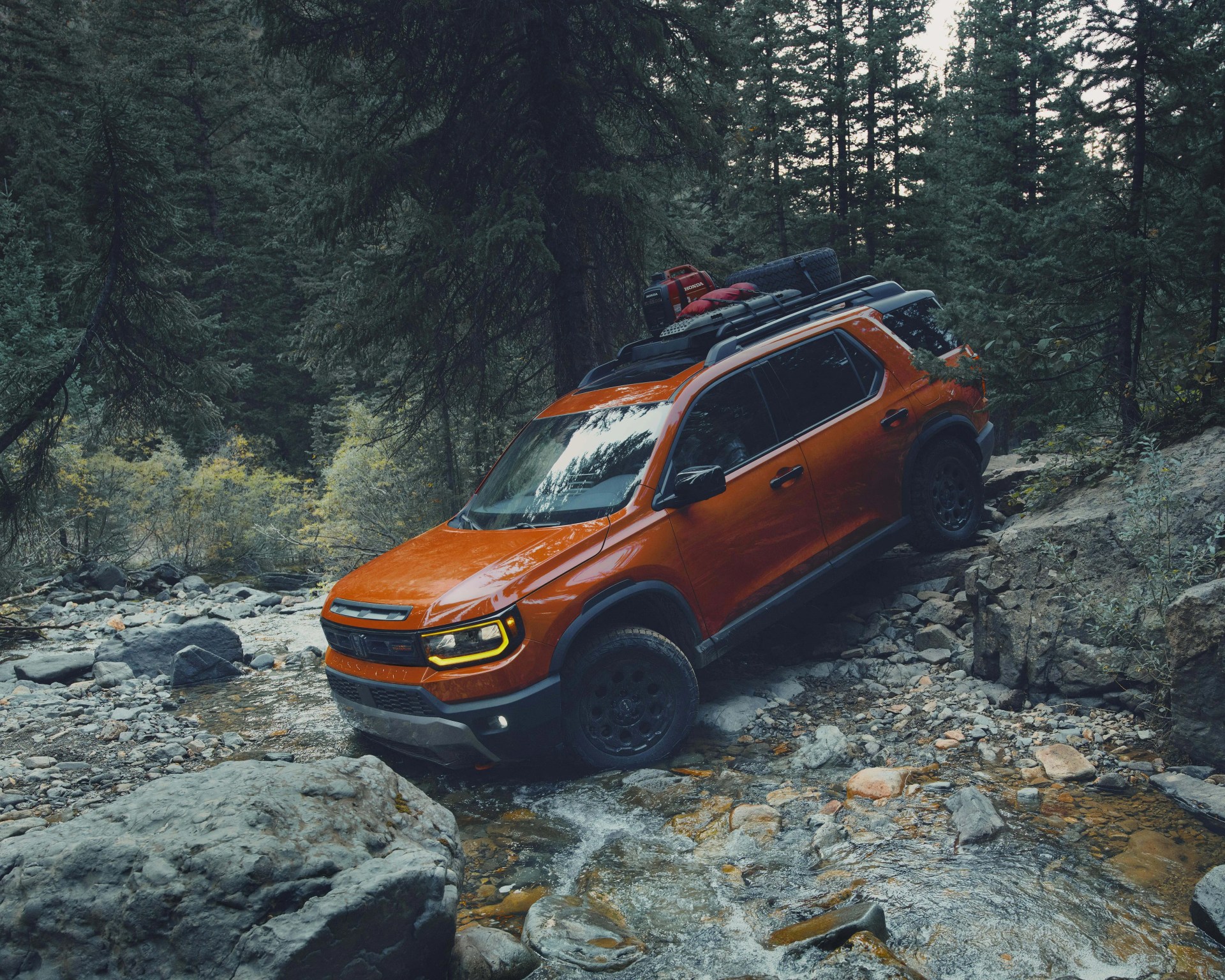 Orange off-road SUV with roof rack and gear crossing rocky stream in forest.
