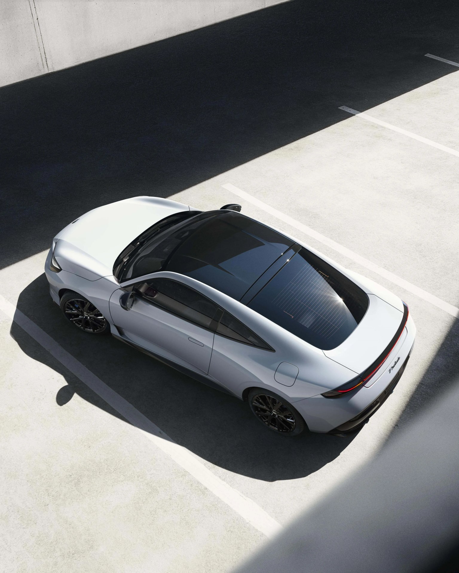 Silver electric sedan with black tinted panoramic roof parked in a sunlit concrete lot.