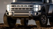 Front view of a matte gray Hyundai off-road vehicle with LED headlights and large rugged tires on rocky terrain.