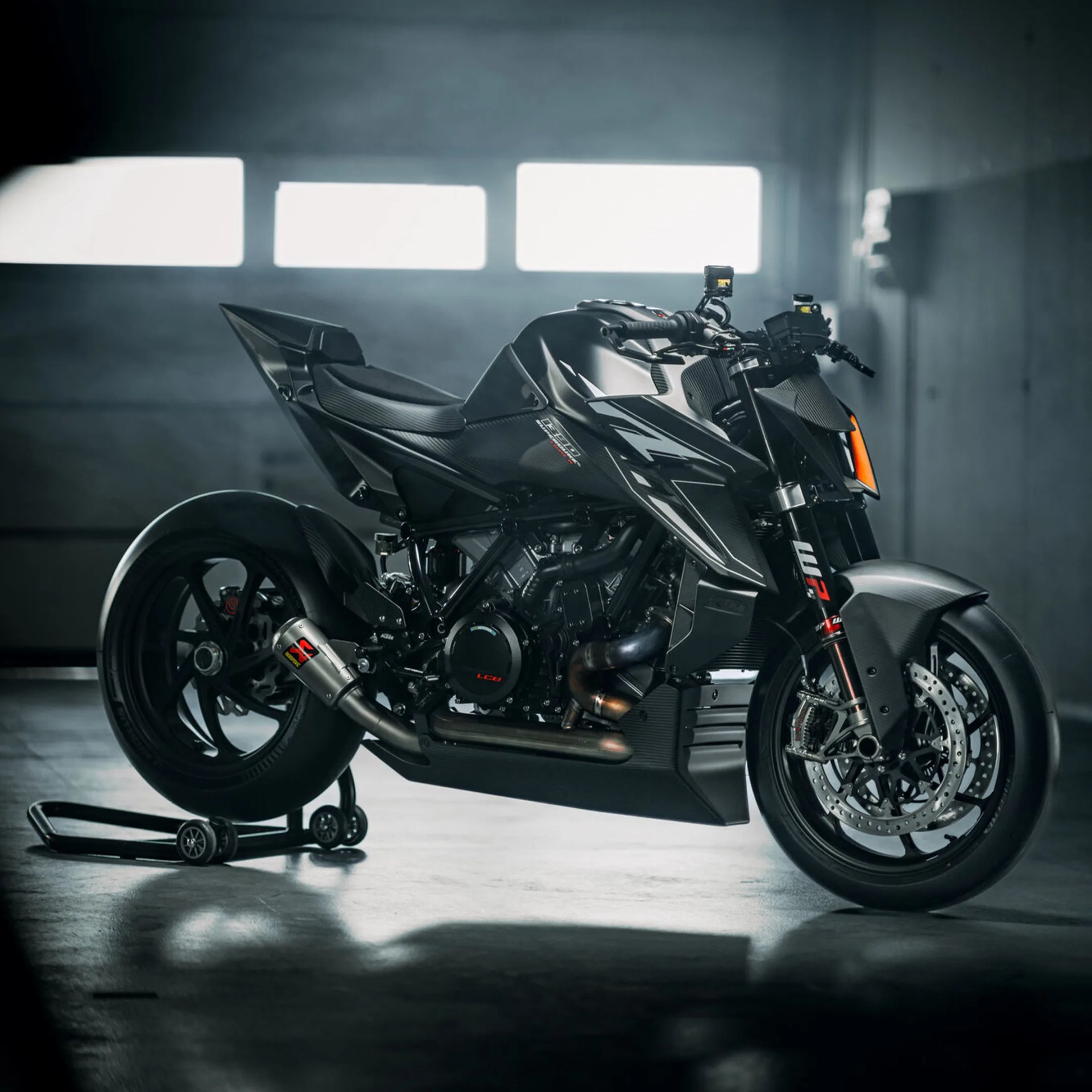 Black sport motorcycle with carbon fiber body panels on a rear wheel stand in a dimly lit garage.