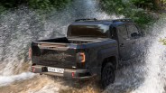 Black pickup truck driving through water splashing on a forest trail.