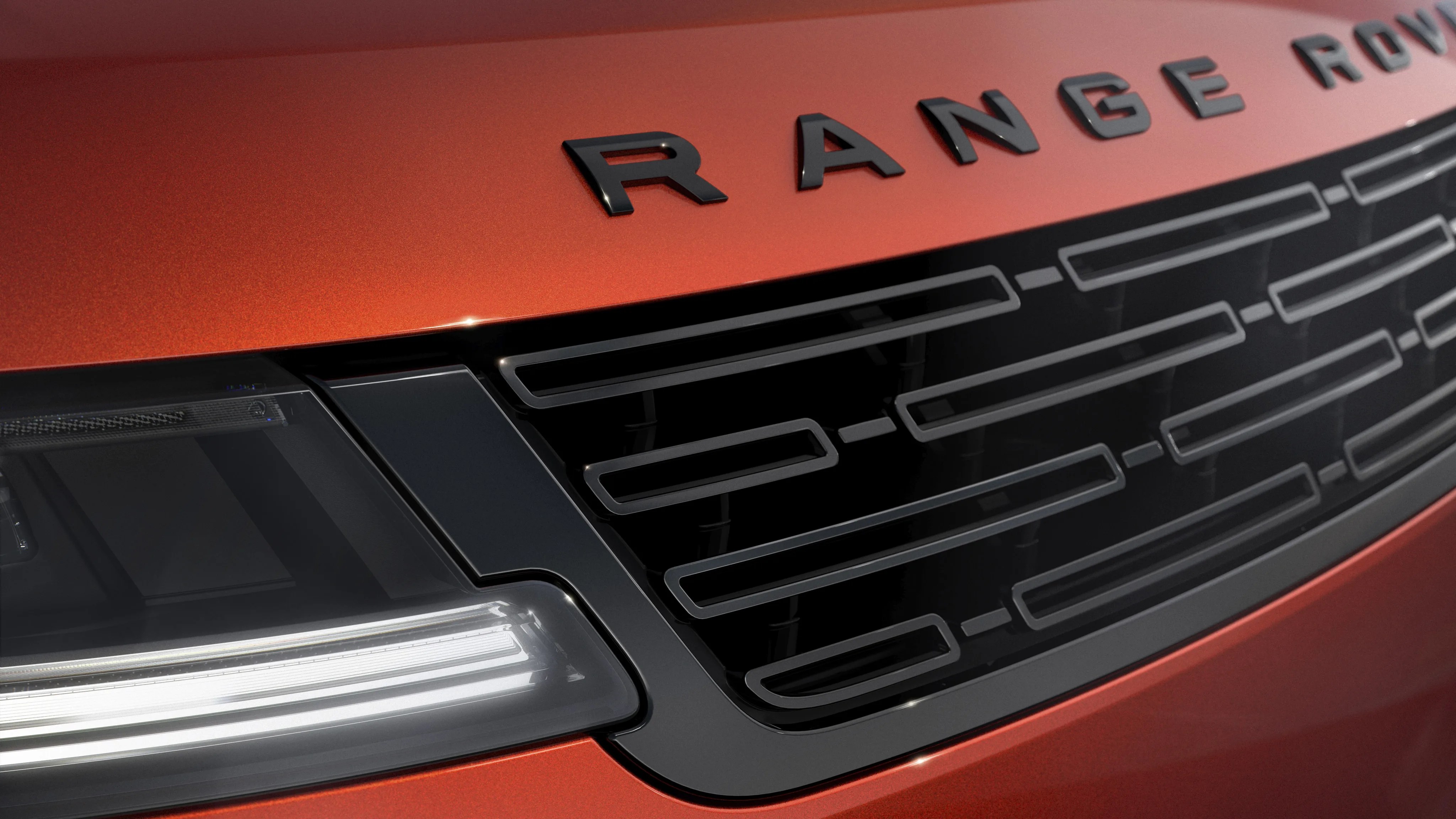 Close-up of a metallic orange Range Rover front grille and headlight with black detailing.
