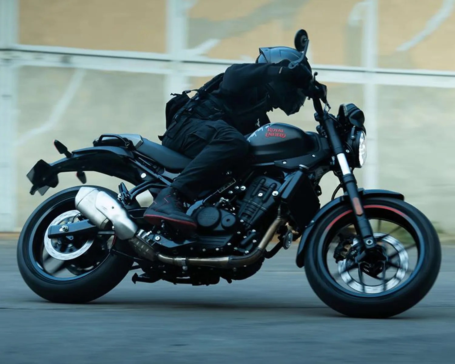 Person in black riding gear leaning forward on a black Royal Enfield motorcycle with red accents.