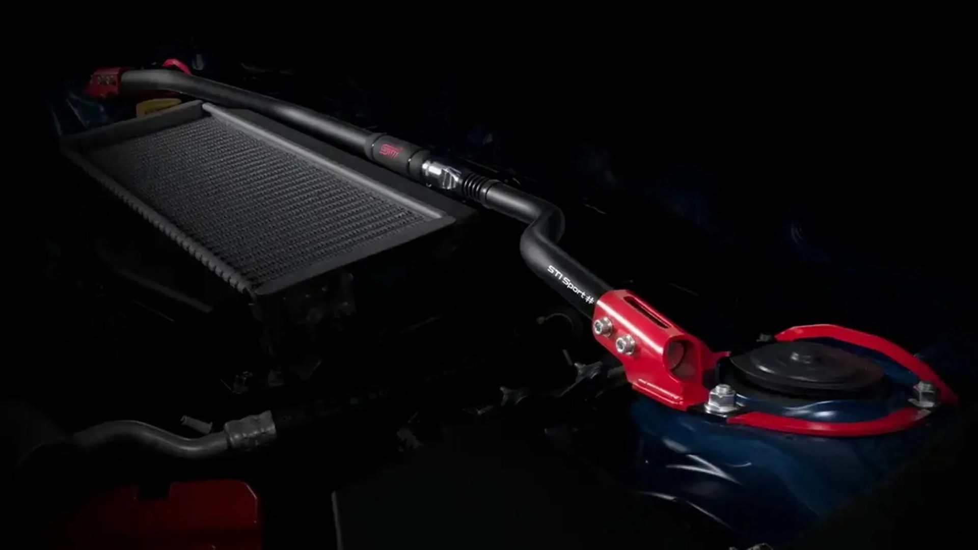 Black and red STI Sport strut tower bar installed in a car engine bay.