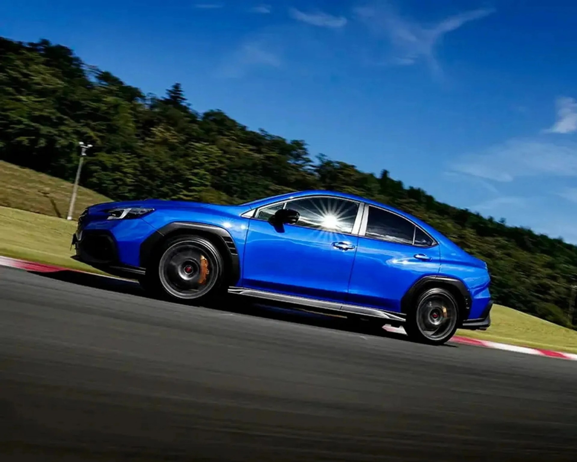 Blue sporty sedan with black wheel arches and tinted windows driving on a race track.