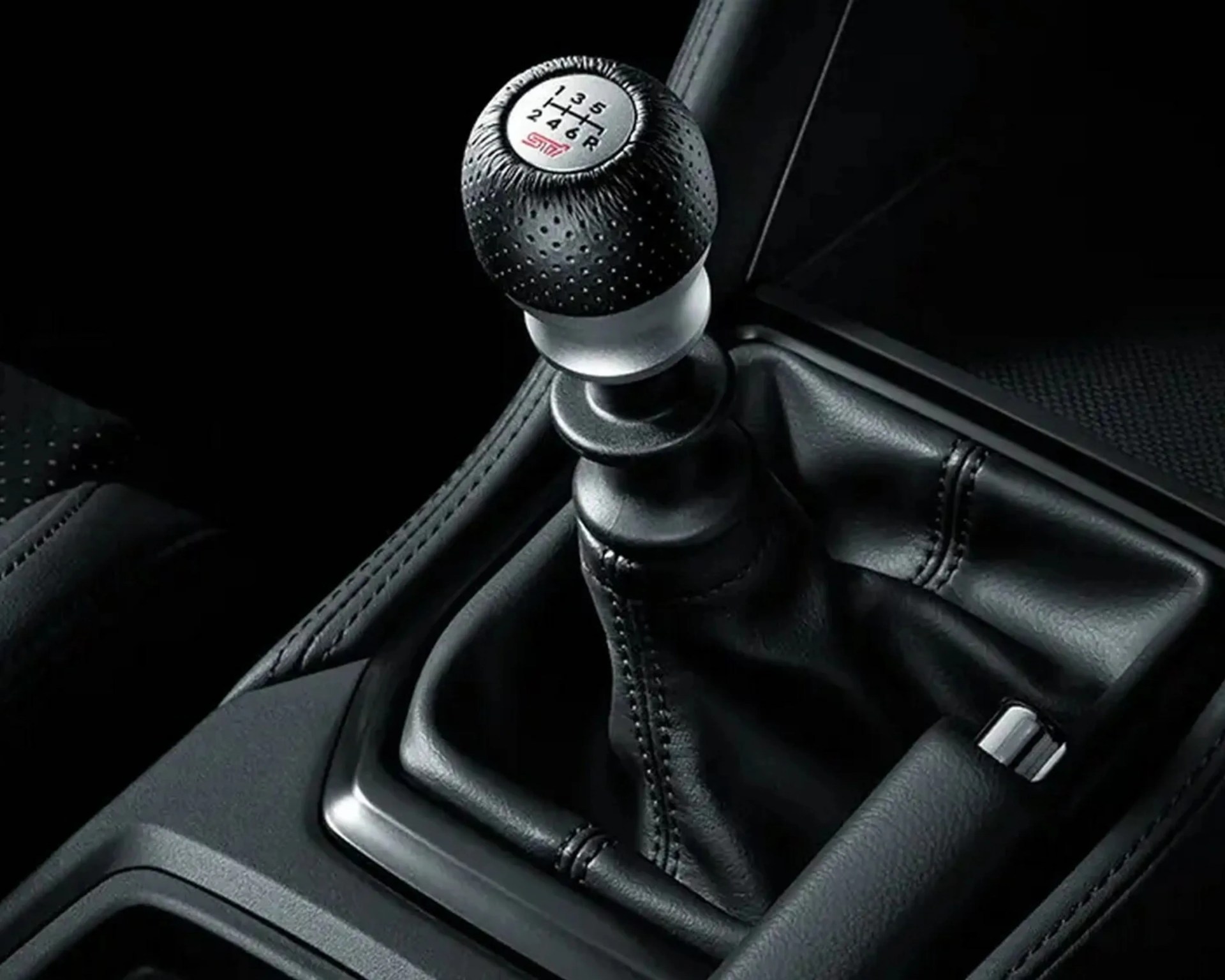Black leather-wrapped manual gear shift knob with silver accent and stitched leather boot in a car interior.