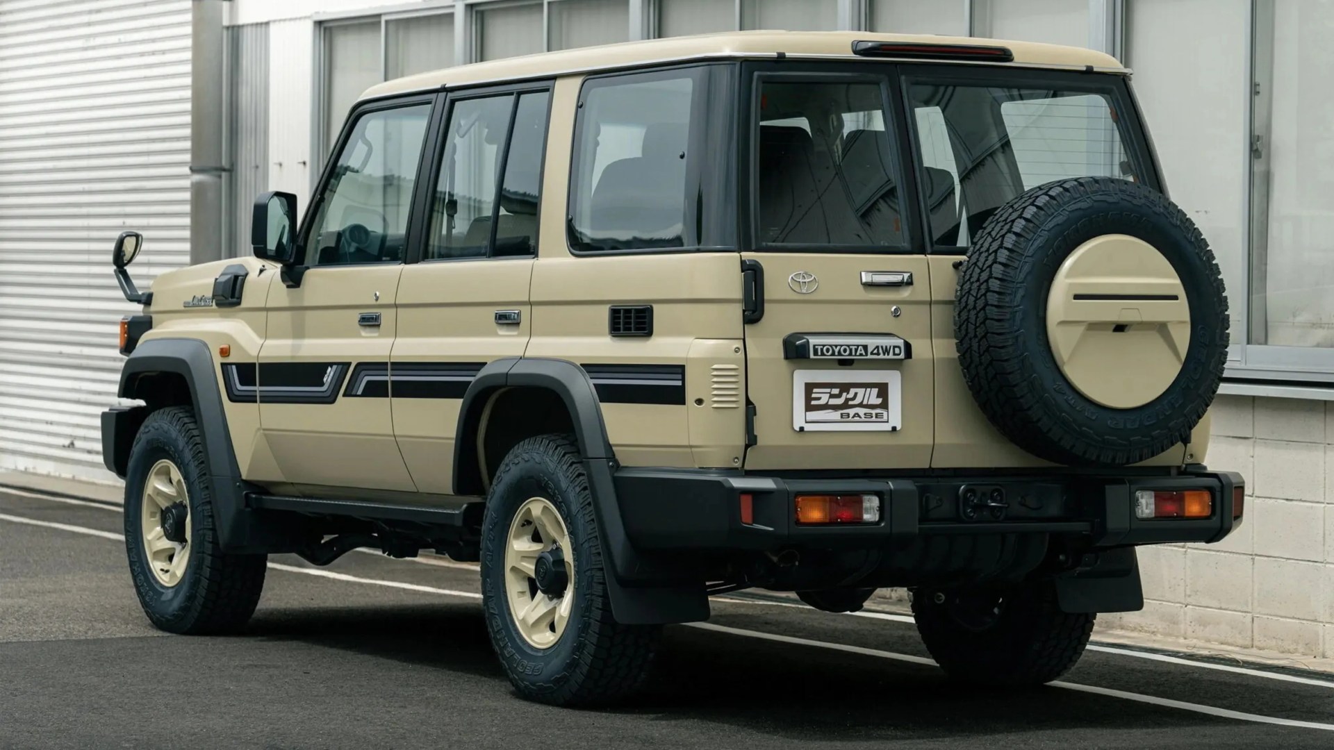 Beige Toyota 4WD SUV with black trim and spare tire mounted on the rear door, parked beside a building.