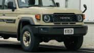 Beige Toyota Land Cruiser with black grille, round headlights, and off-road tires parked by a white wall.