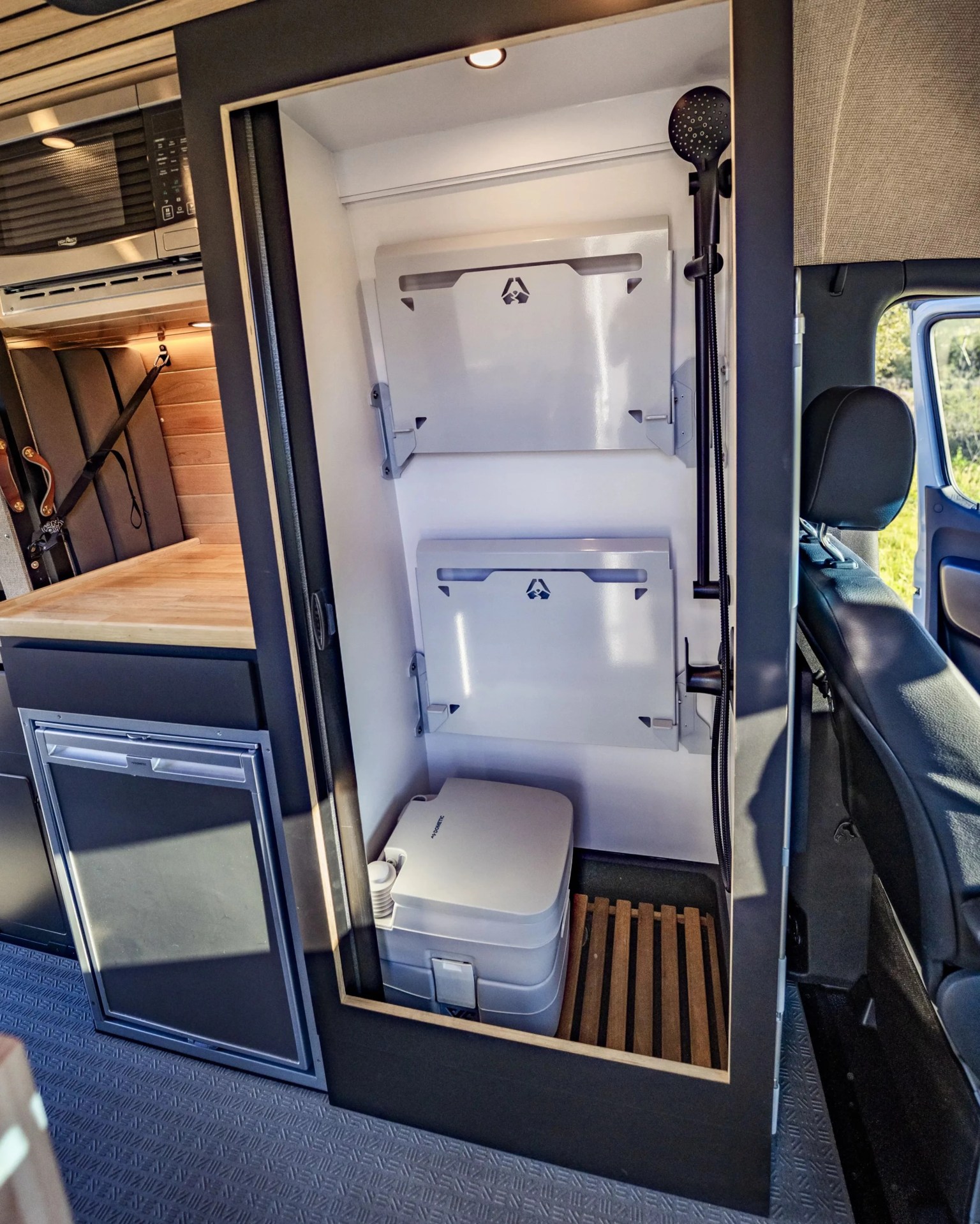 Compact portable toilet with two foldable white panels and a black showerhead inside a camper van bathroom.