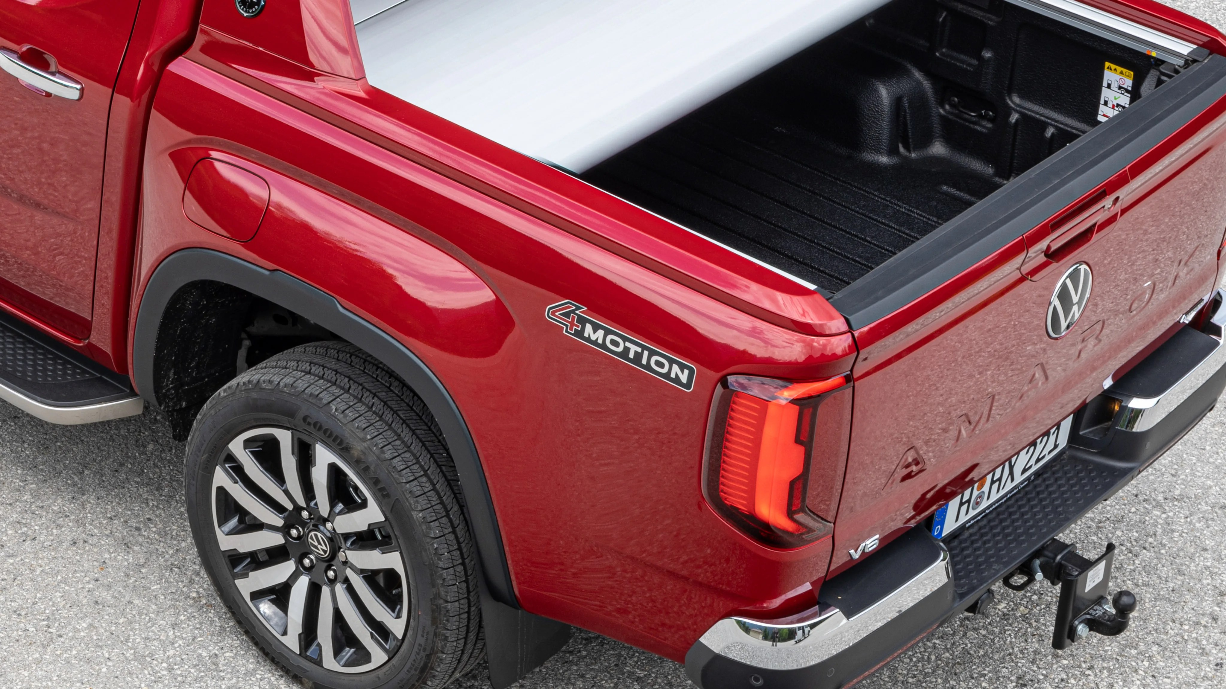 Red Volkswagen Amarok pickup truck rear side with 4MOTION badge, V6 emblem, and black bed liner.