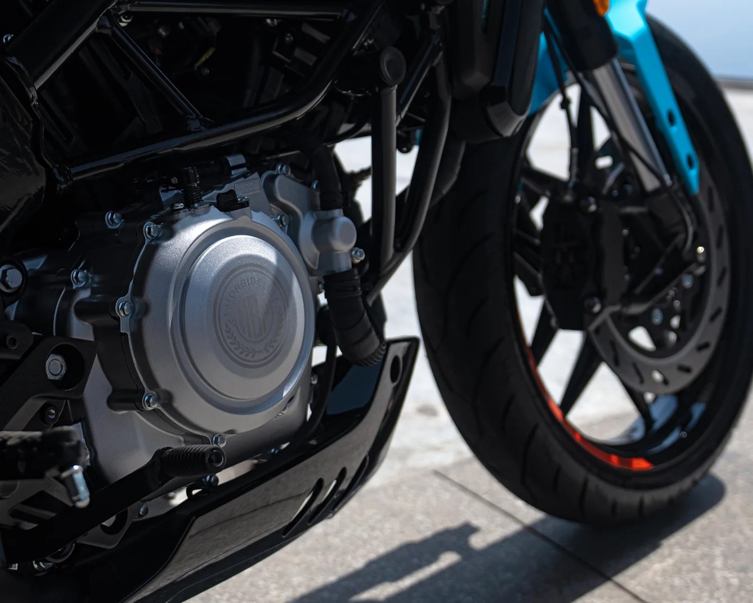 Close-up of a motorcycle engine and front wheel with a blue fork and black tire on a tiled surface.