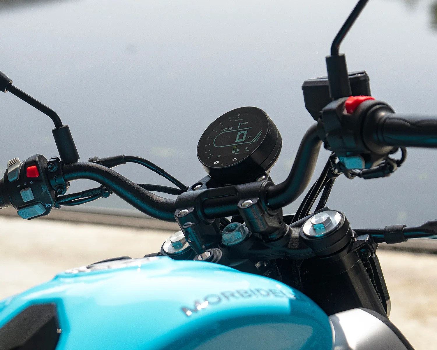 Close-up of a motorcycle's black handlebars with a digital speedometer and a blue fuel tank.