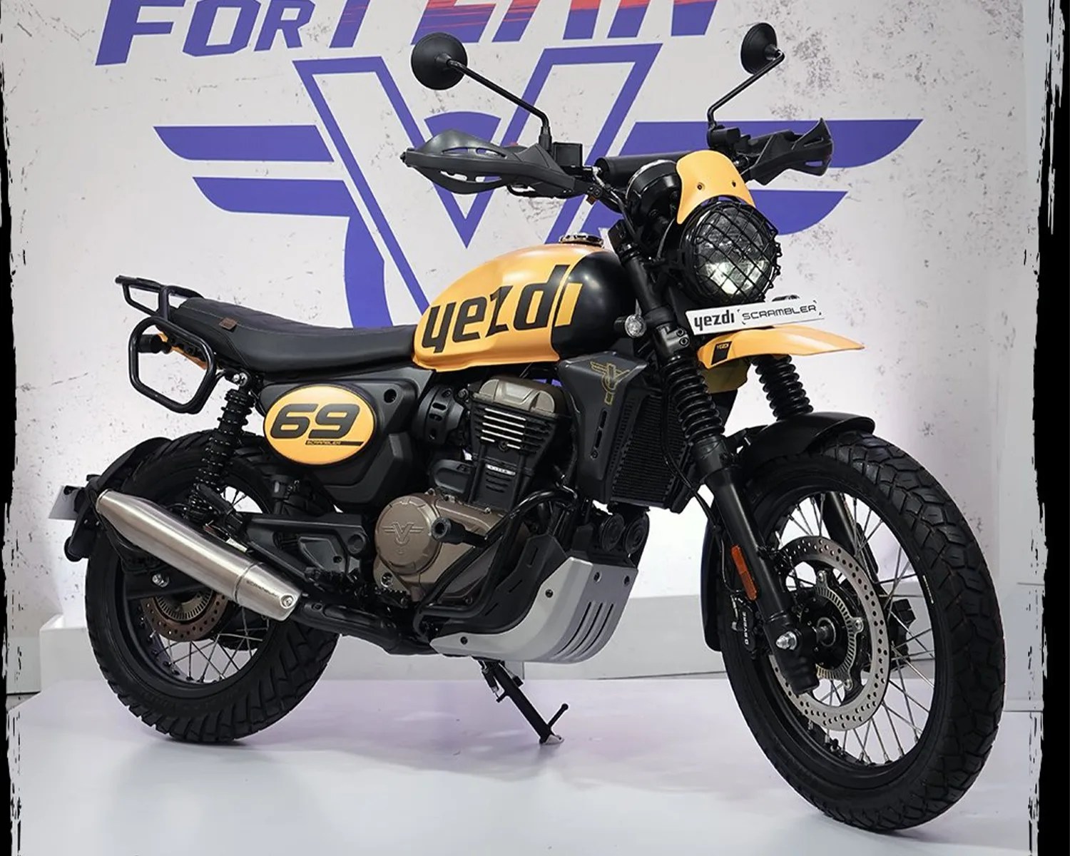 Yellow and black Yezdi Scrambler motorcycle with knobby tires and protective headlight grill.