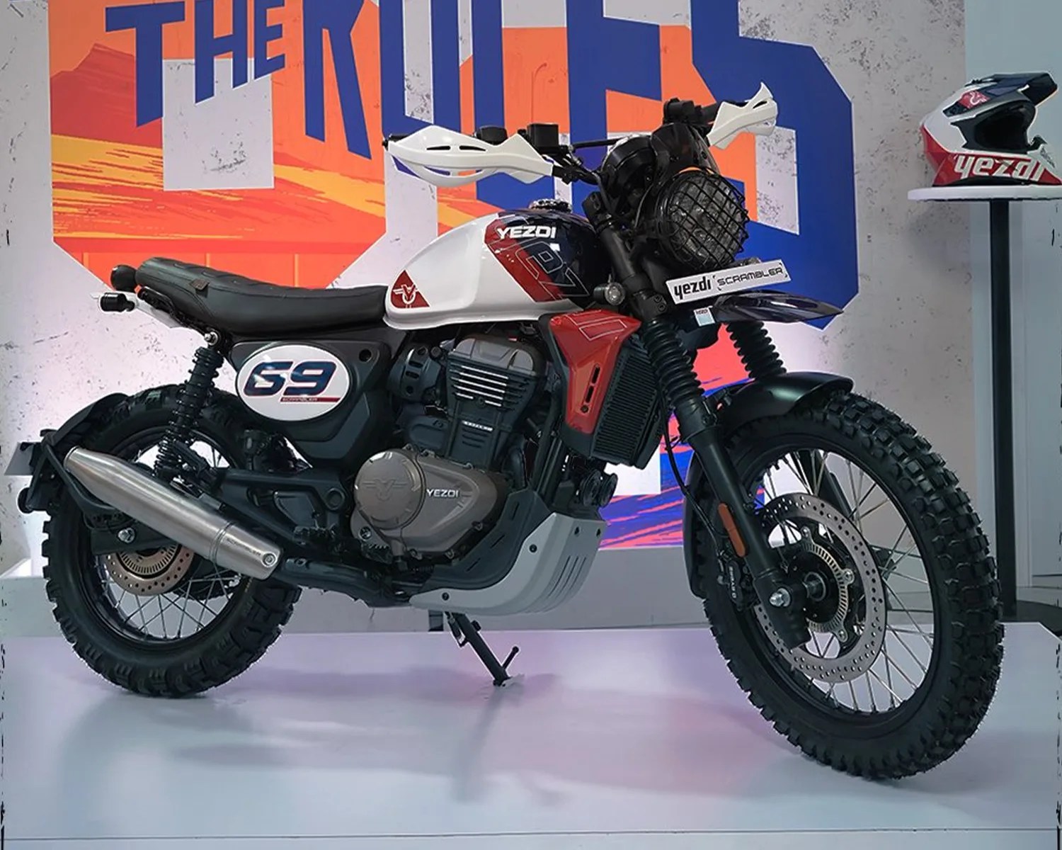 White and red Yezdi Scrambler motorcycle with knobby tires and a black seat on display.