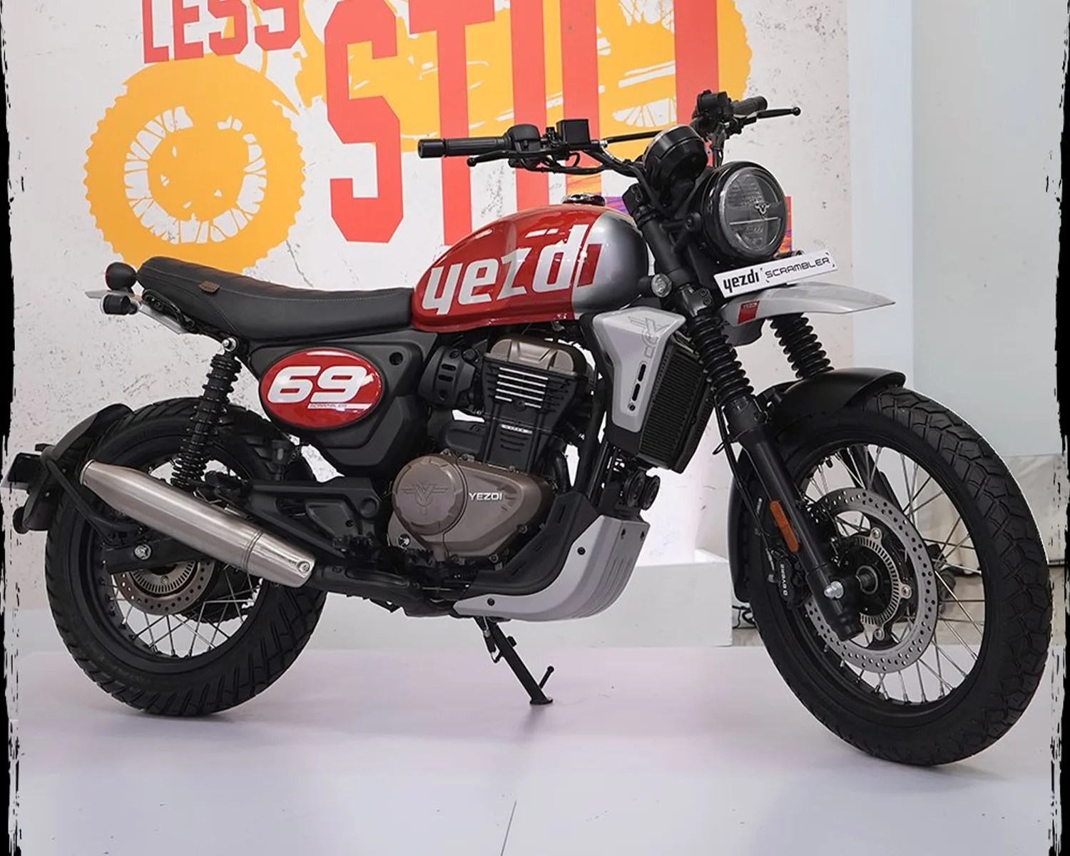 Red and silver Yezdi Scrambler motorcycle with black seat and tires on a white floor.