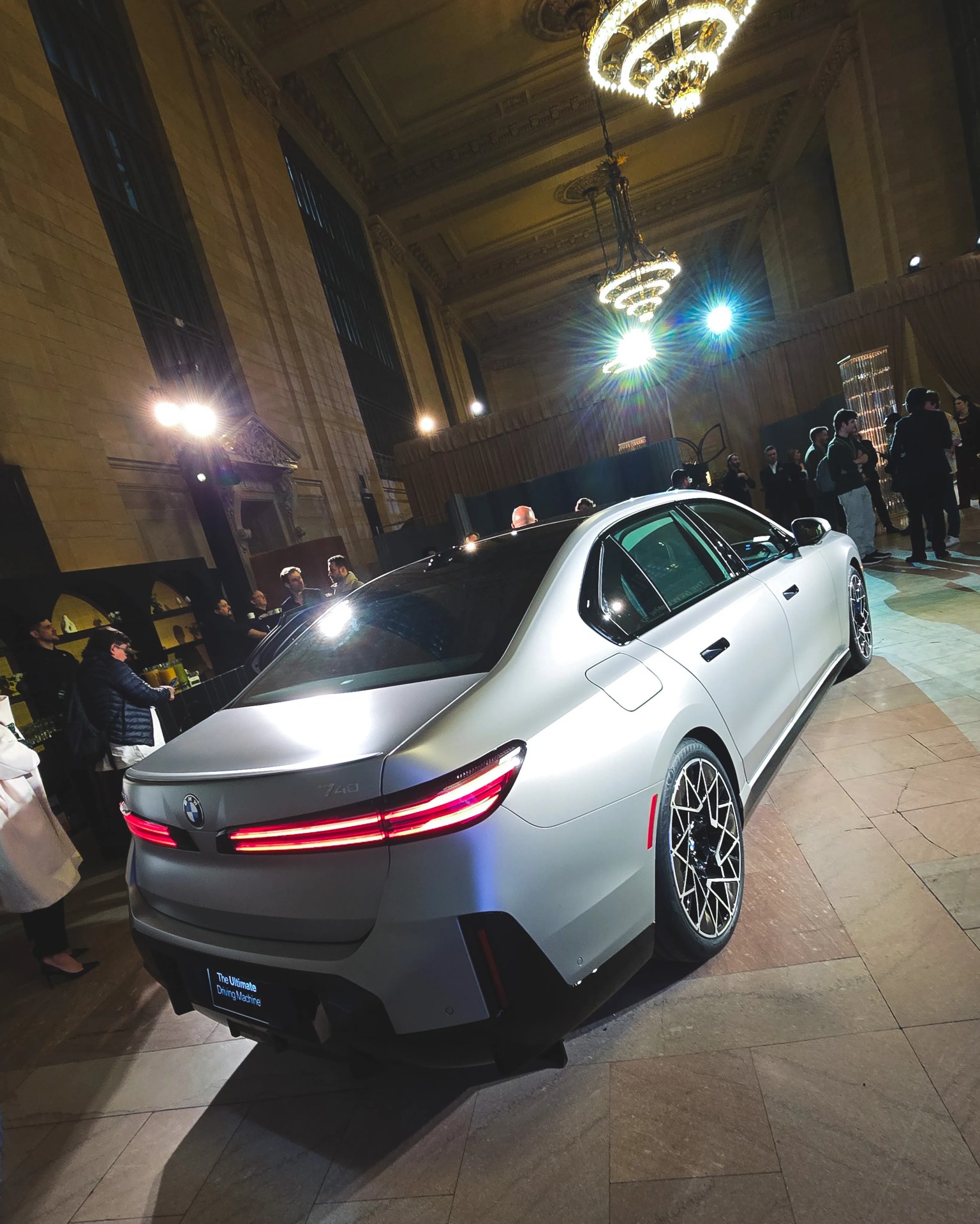 Silver BMW 740 sedan with illuminated taillights displayed indoors under chandeliers.