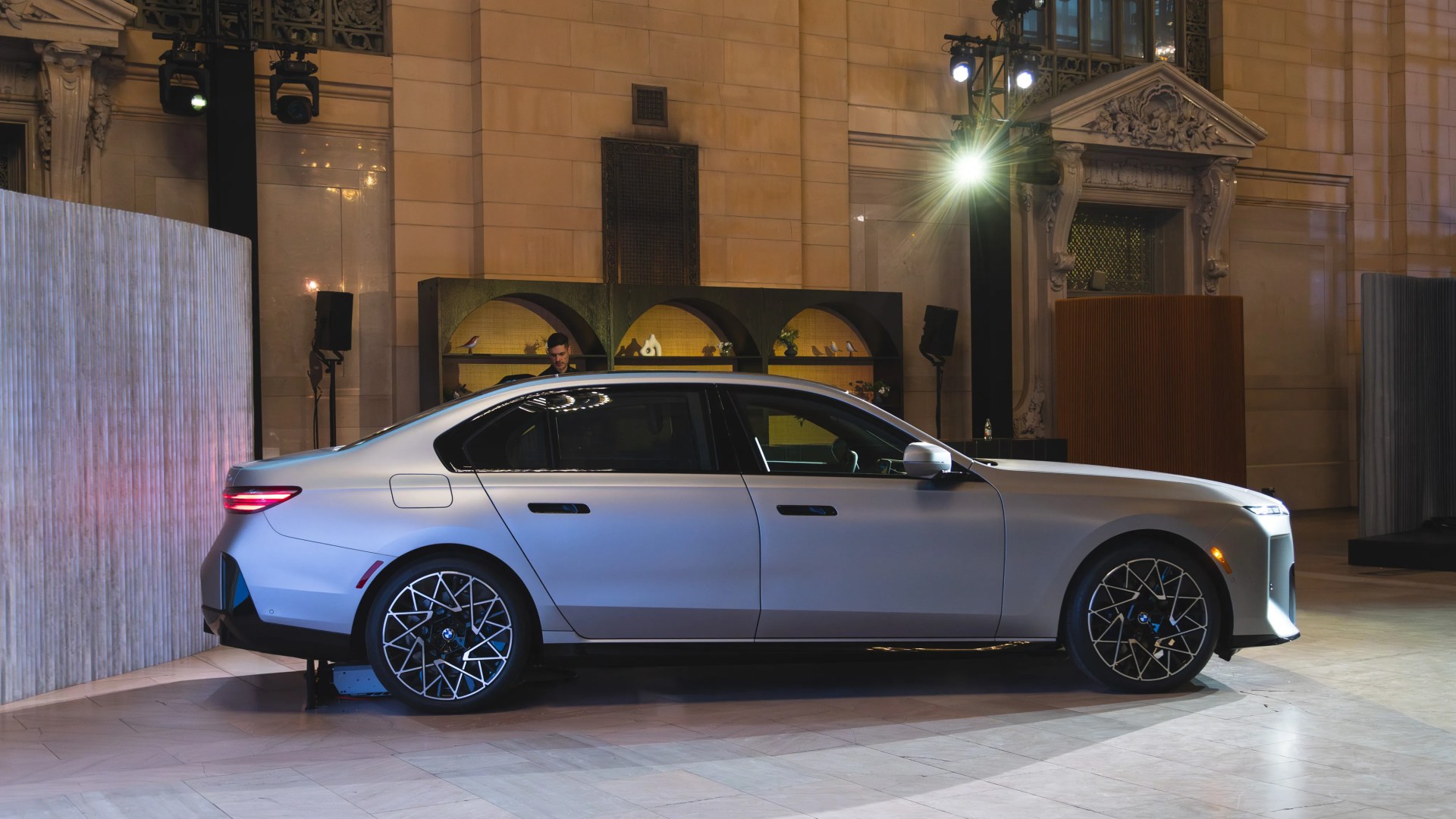 Silver BMW sedan with black and silver multi-spoke wheels displayed indoors under bright lights.