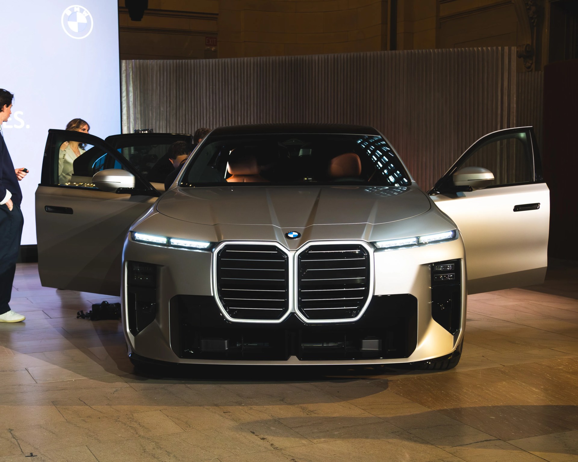 Front view of a silver BMW SUV with open front doors and illuminated headlights indoors.