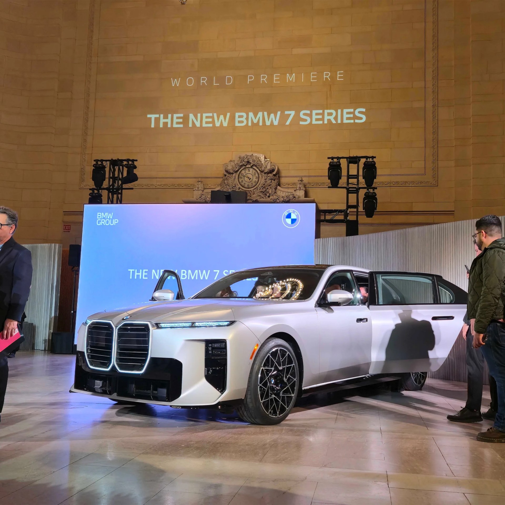Silver BMW 7 Series sedan with large kidney grille and black multi-spoke wheels at an indoor event.