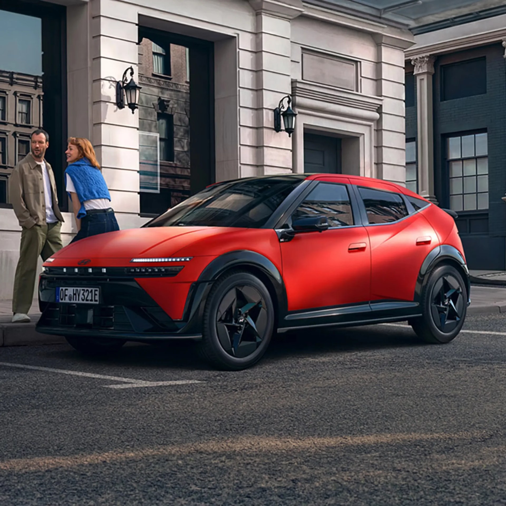 Red compact crossover SUV with black roof and wheels parked on a city street near a building entrance.