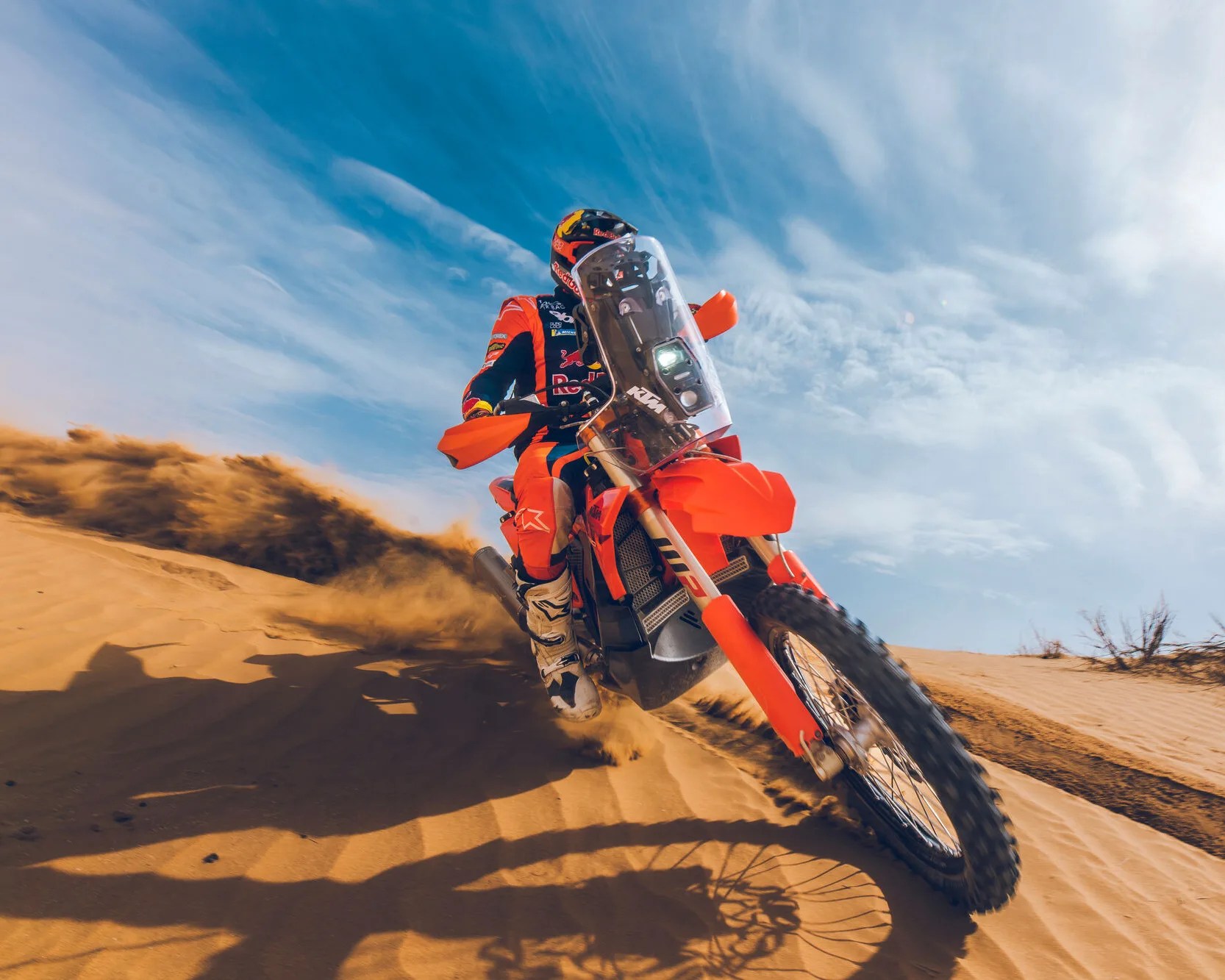 Orange KTM dirt bike kicking up sand in a desert with a rider in matching orange and black gear.