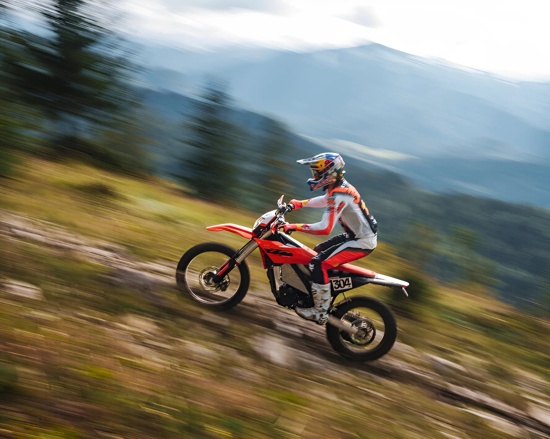 Person wearing a helmet riding a red dirt bike uphill on a blurred outdoor trail.