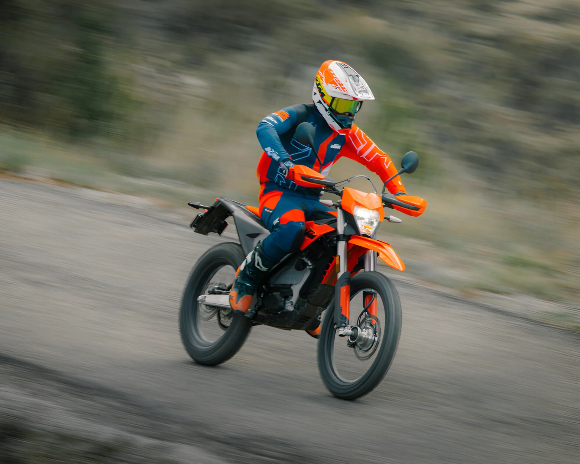 Person wearing orange and blue riding gear and helmet riding an orange off-road motorcycle on a dirt path.