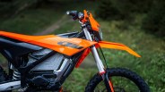 Close-up of the front and side of an orange and black KTM dirt bike with knobby tires on a grassy background.