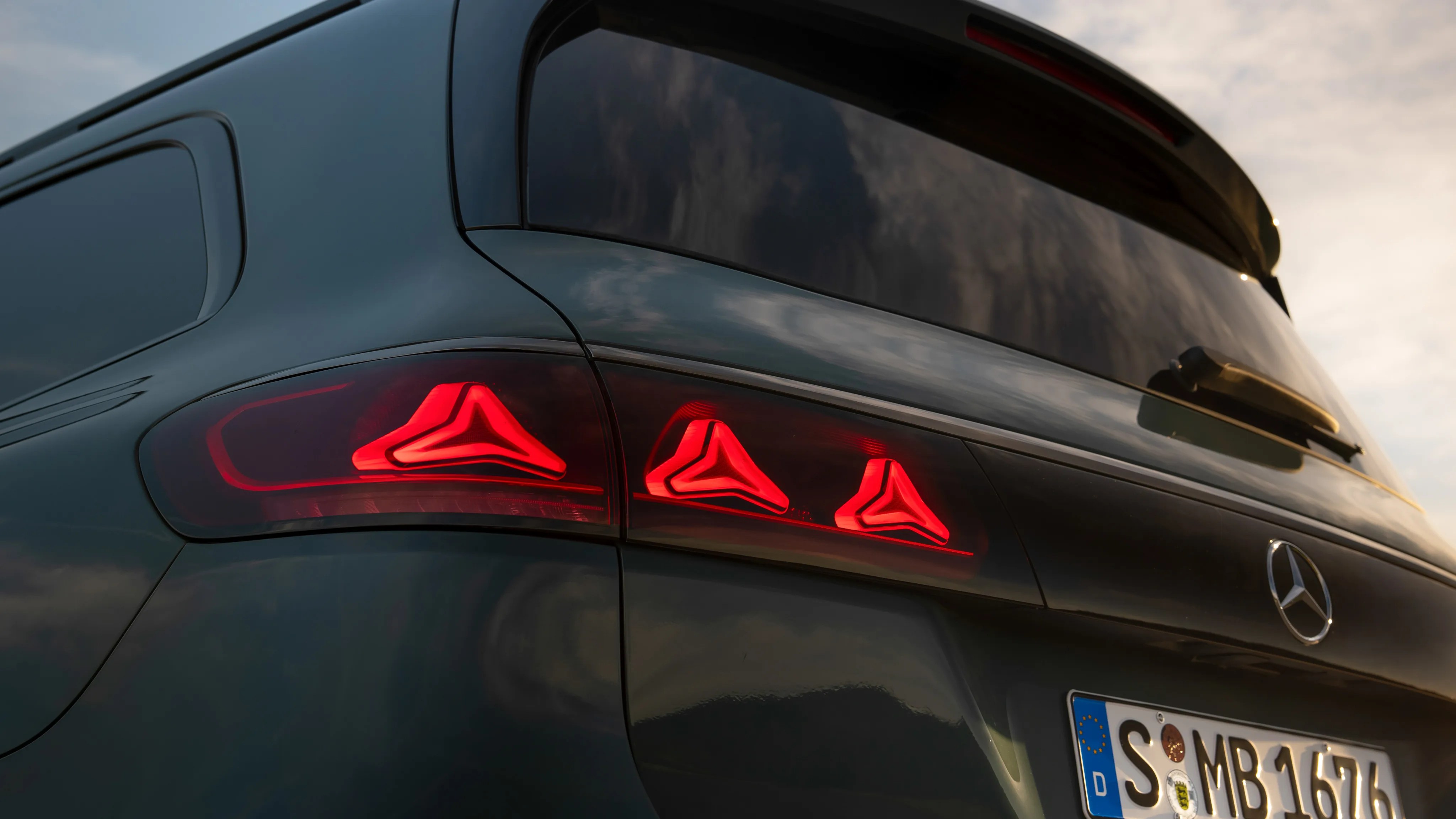 Rear view of a dark green Mercedes-Benz vehicle with illuminated red triangular taillights and a European license plate.
