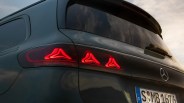 Rear view of a dark green Mercedes-Benz vehicle with illuminated red triangular taillights and a European license plate.