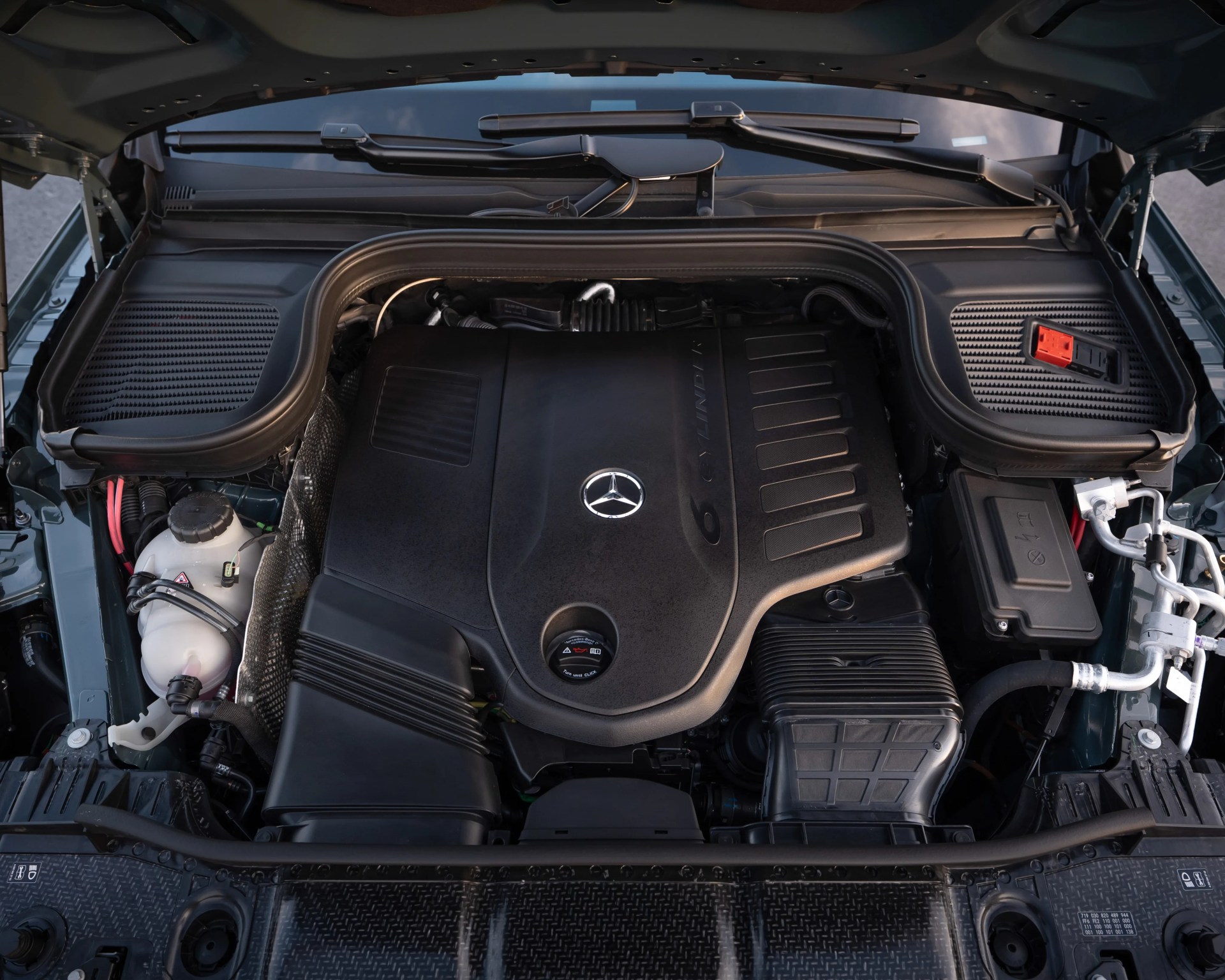 Engine compartment of a Mercedes-Benz vehicle with a large black engine cover featuring the Mercedes logo.