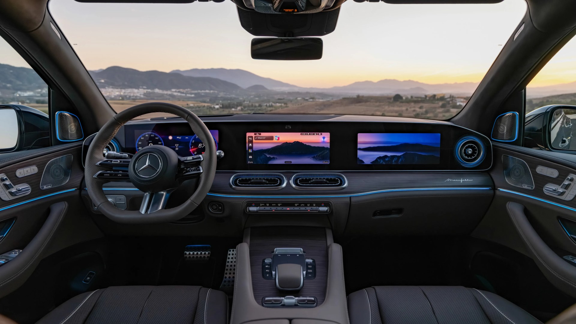 Interior of a Mercedes-Benz car featuring a digital dashboard with three screens, wood trim, and ambient blue lighting.