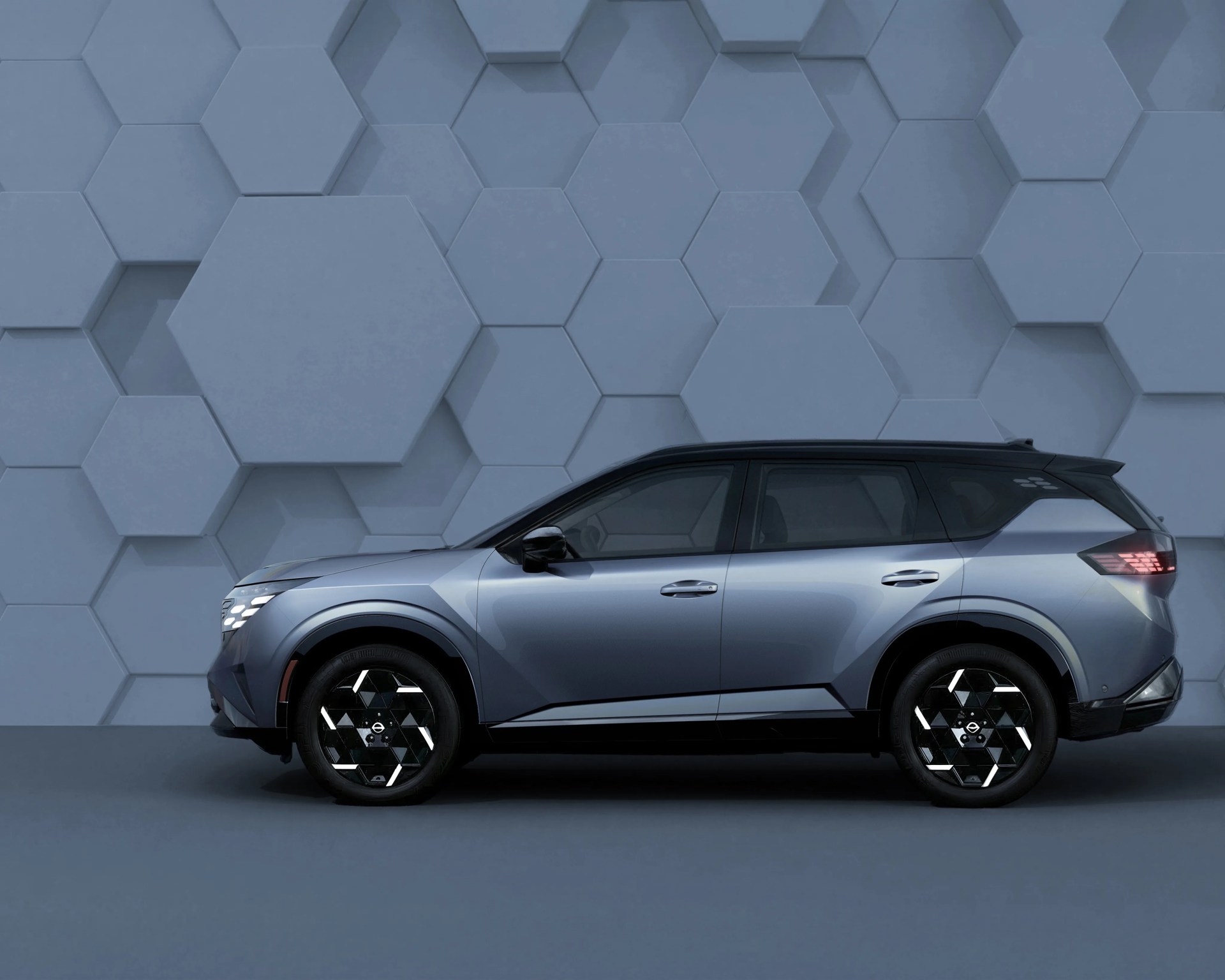 Side view of a metallic blue SUV with black geometric-patterned wheels against a blue hexagonal textured wall.