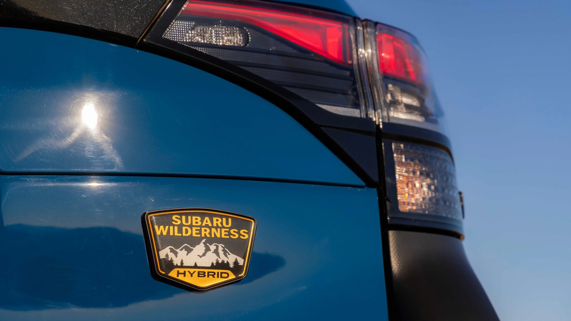 Close-up of a blue Subaru vehicle's rear with a "Subaru Wilderness Hybrid" badge and part of the taillight visible.