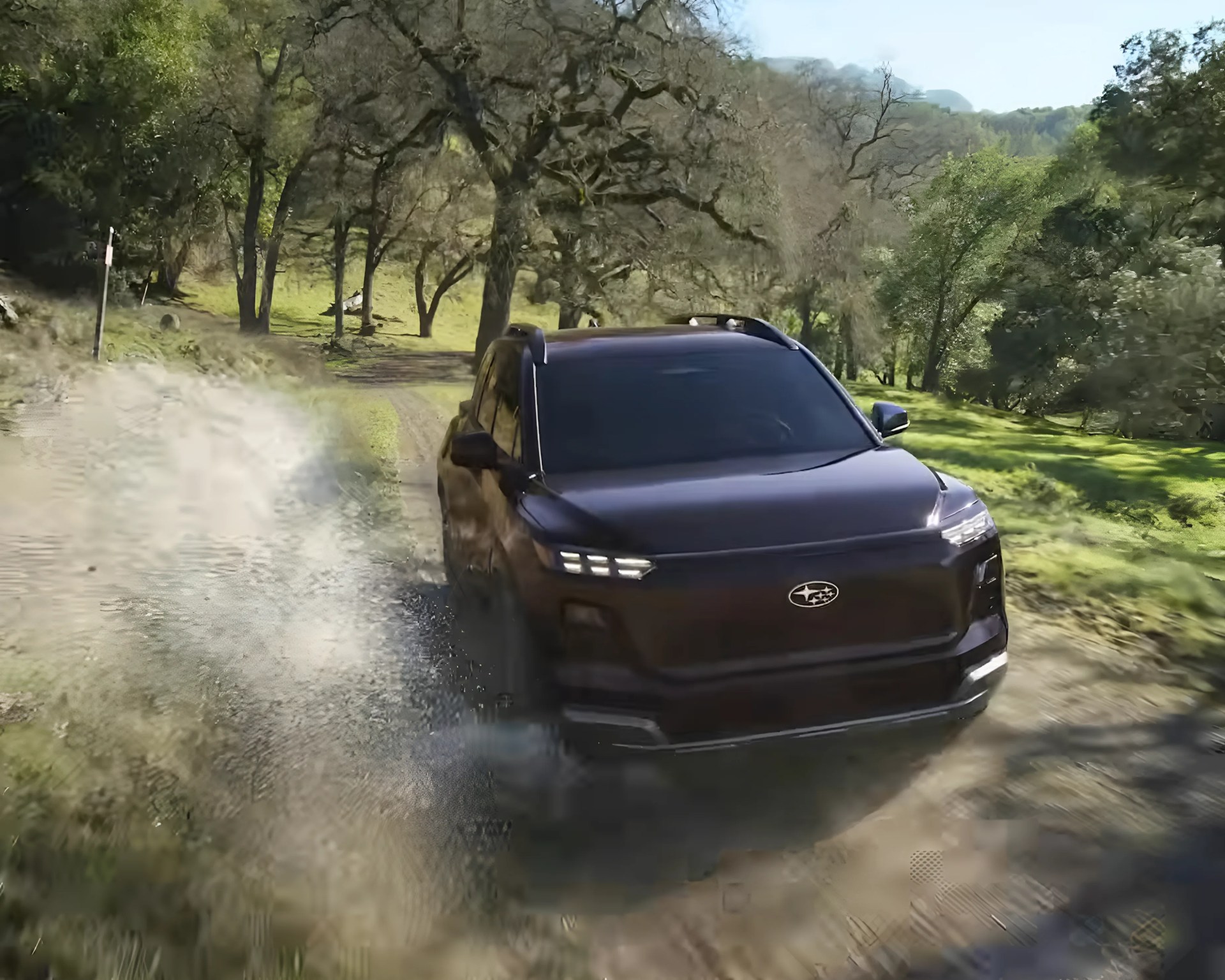 Black Subaru SUV kicking up dust on a dirt road surrounded by green trees and hills.