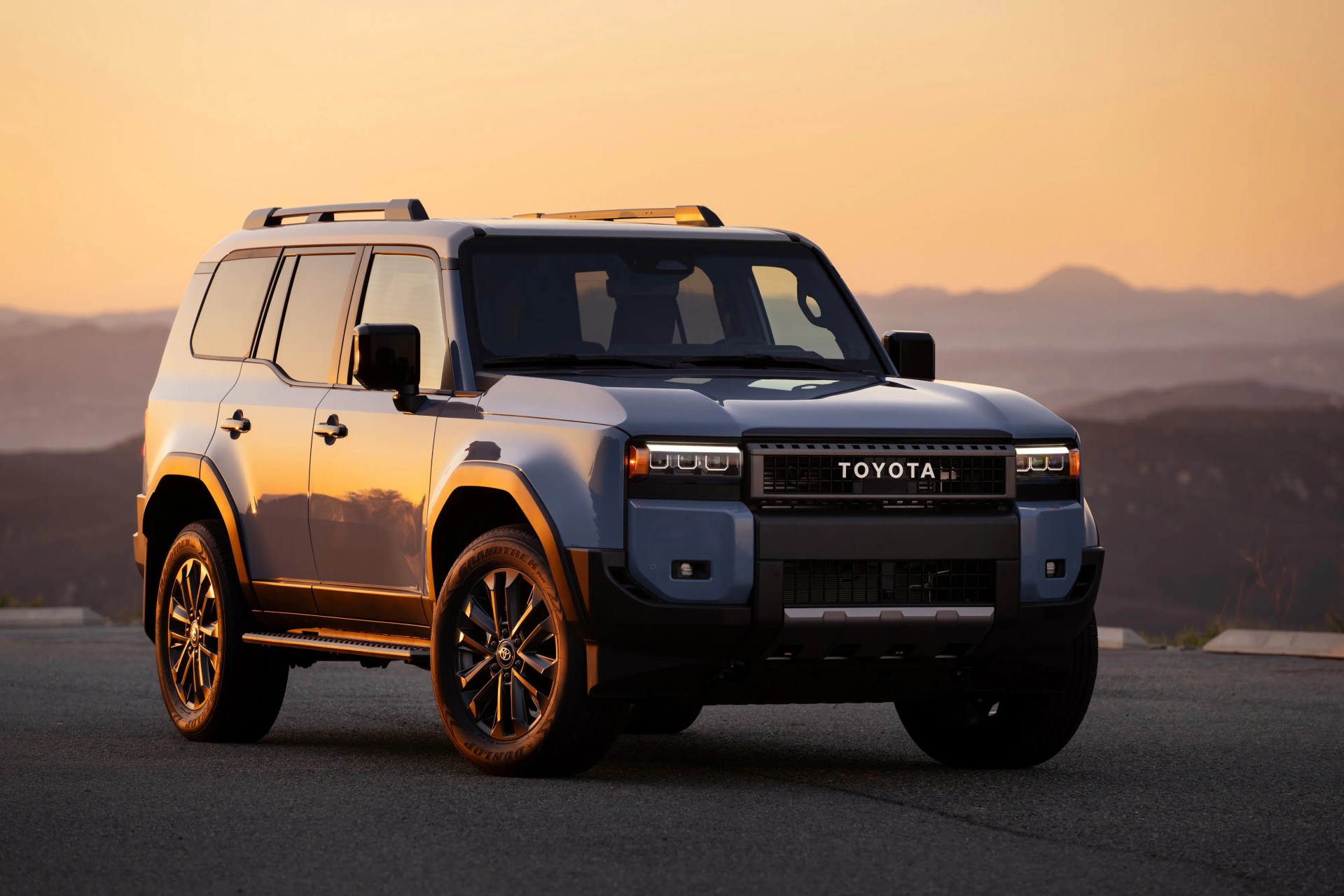 Blue Toyota SUV with black grille and roof rails parked on asphalt at sunset.