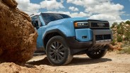 Blue Toyota SUV with black trim and grille parked on a dirt trail near large rocks under a partly cloudy sky.
