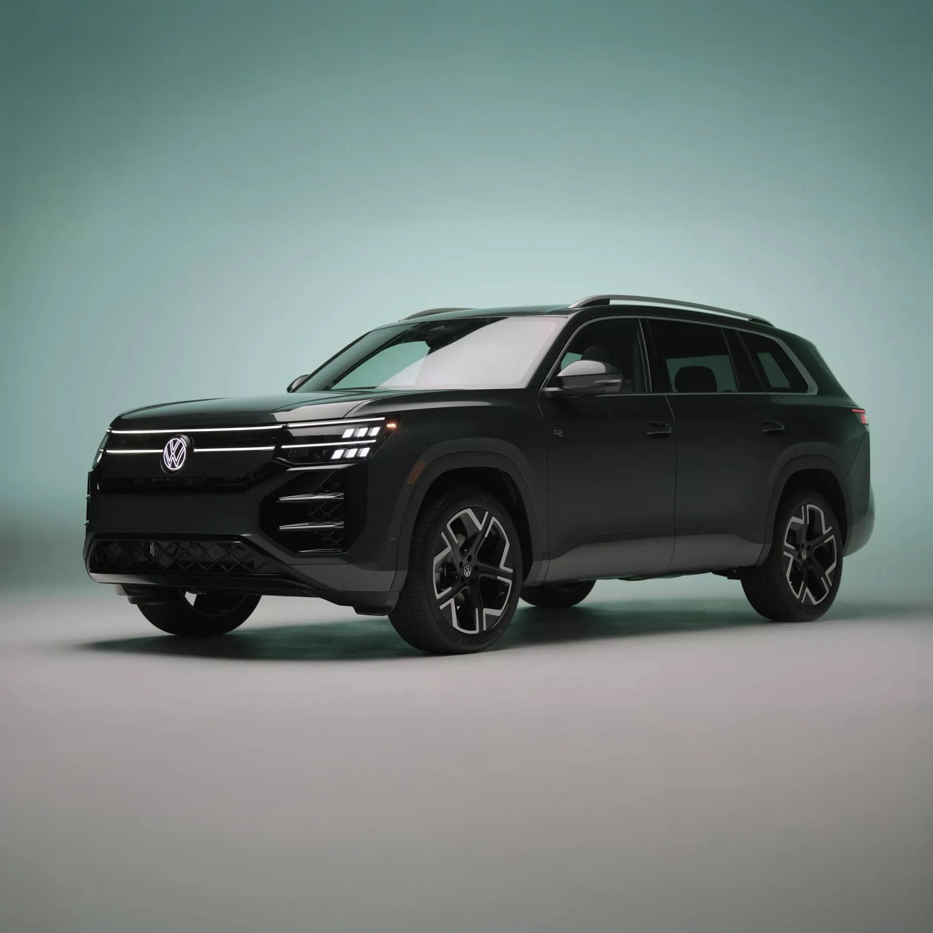 Black Volkswagen SUV with LED headlights and large alloy wheels on a plain light green background.