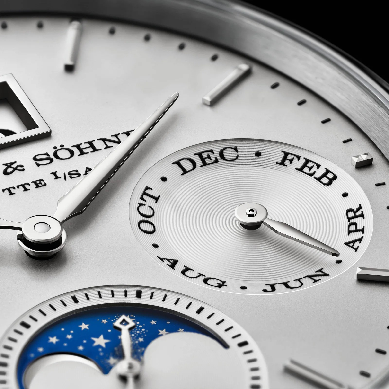 Close-up of a silver watch face showing month indicator with months in black text and a blue moon phase dial.