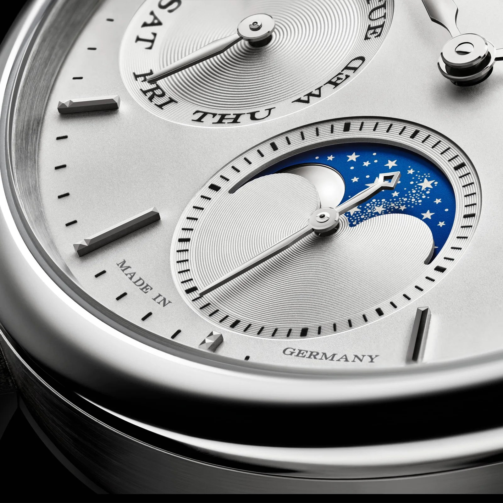 Close-up of a silver watch face showing day and moon phase subdials with "Made in Germany" text.