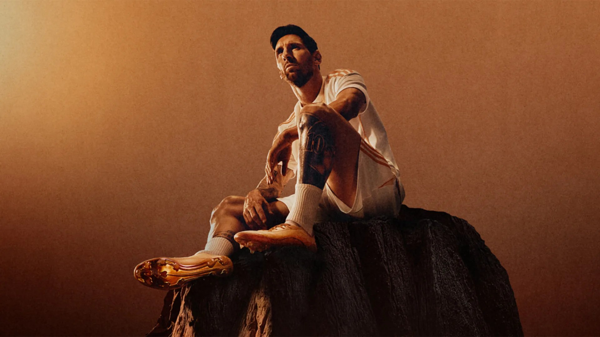 Man in white sportswear and golden cleats sitting on a large rock against a brown gradient background.