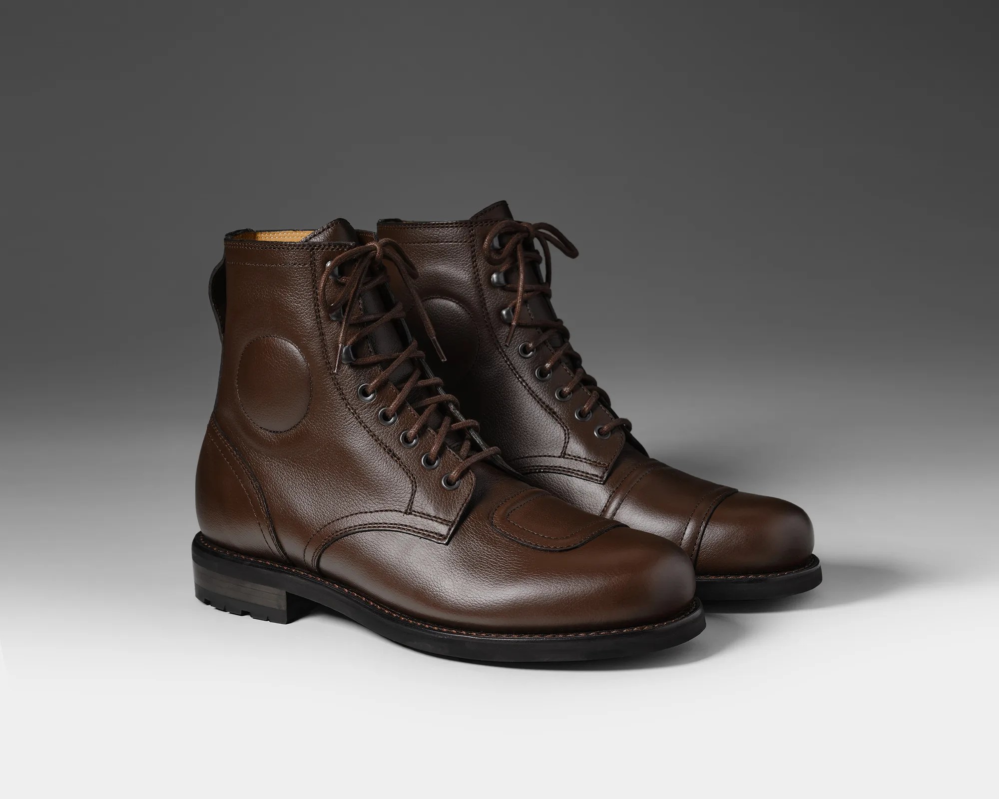 Pair of dark brown leather lace-up boots with round patches on the sides and black soles.