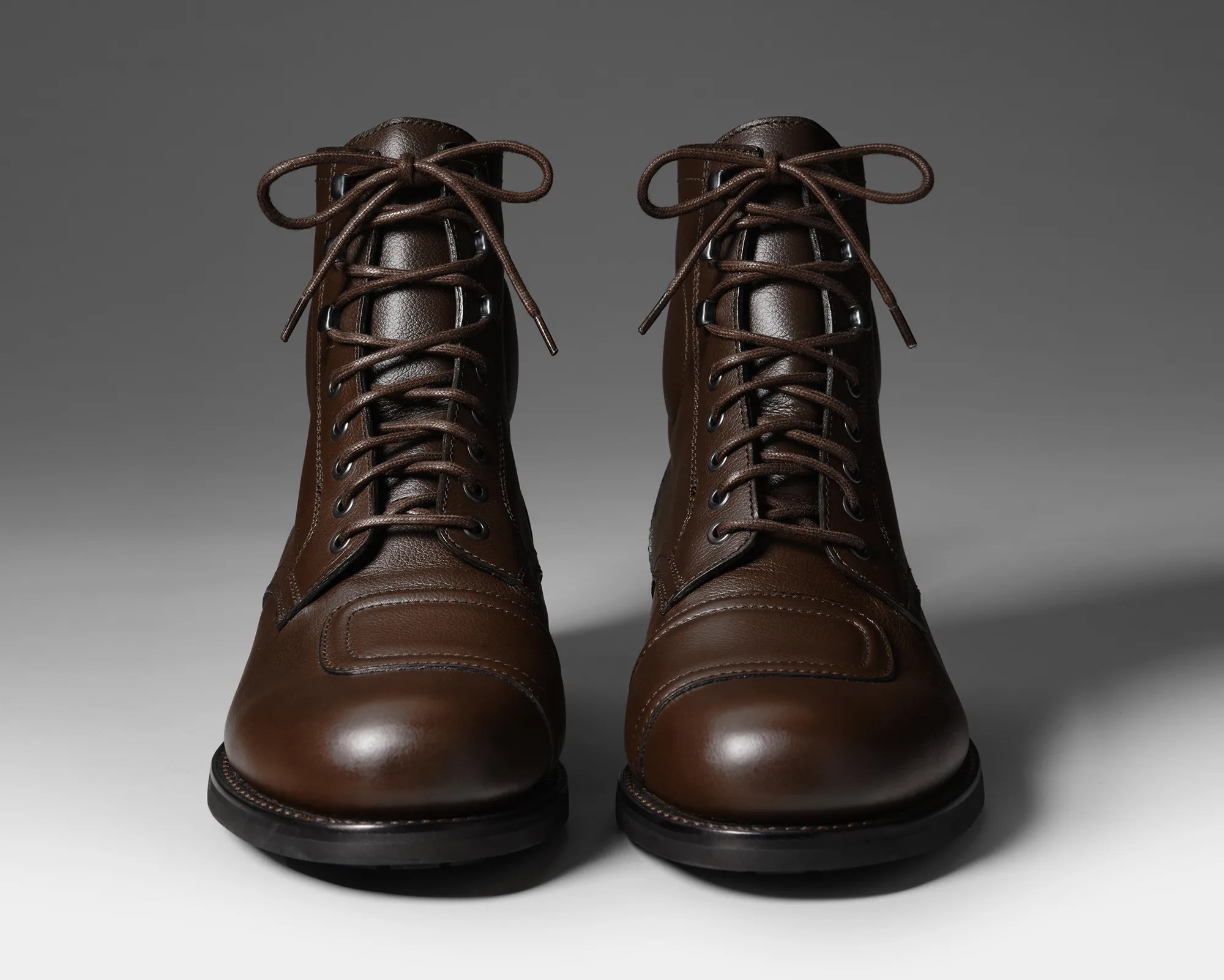 Pair of brown leather lace-up boots with black soles on a gray gradient background.