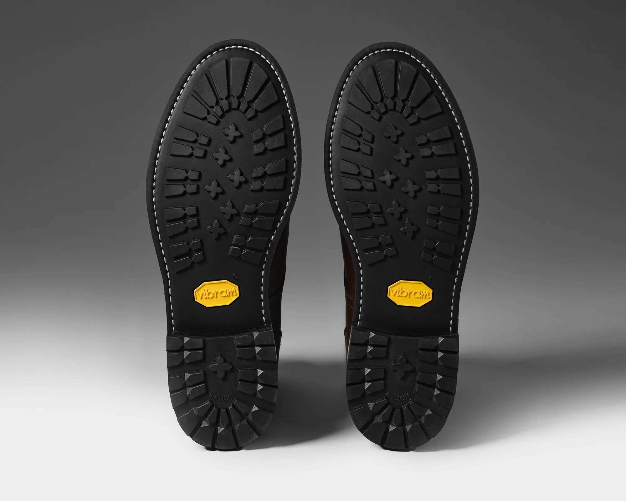 Black Vibram rubber soles with deep treads and white stitching around the edges.