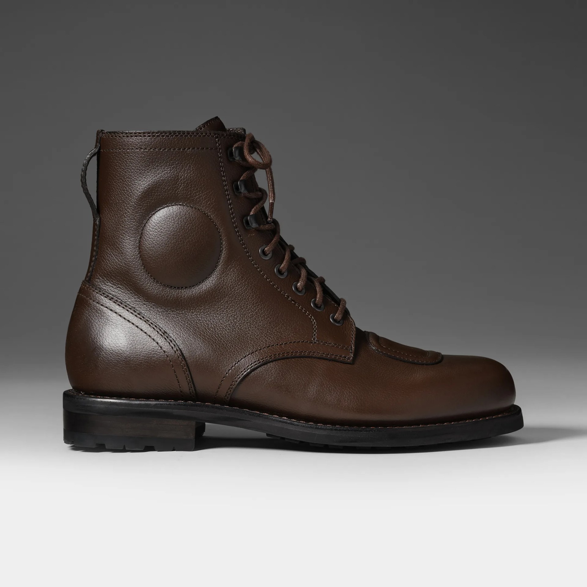 Brown leather lace-up boot with round padded detail on the side and black sole.