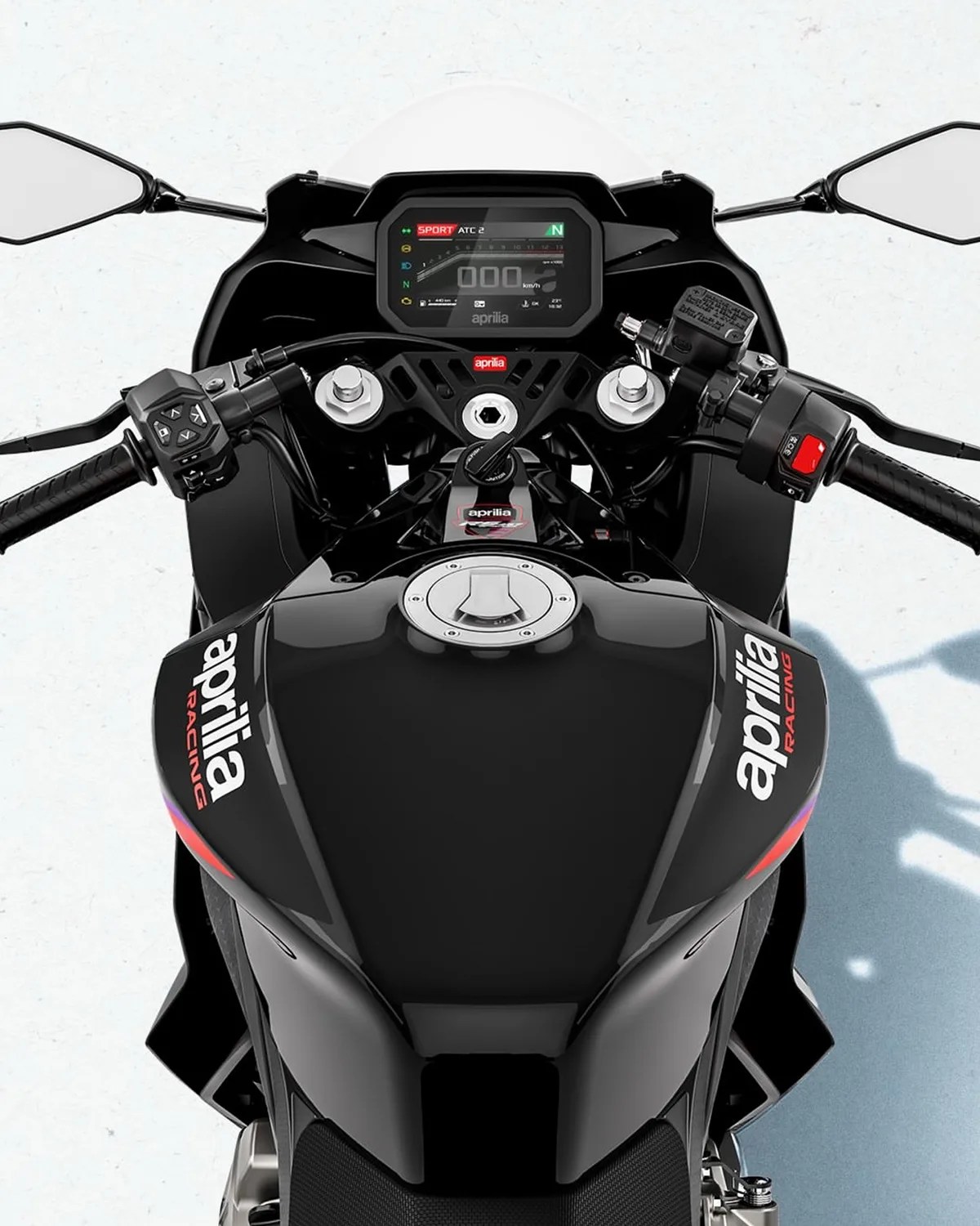 Top view of a black Aprilia Racing motorcycle dashboard and fuel tank with digital display and handlebars.